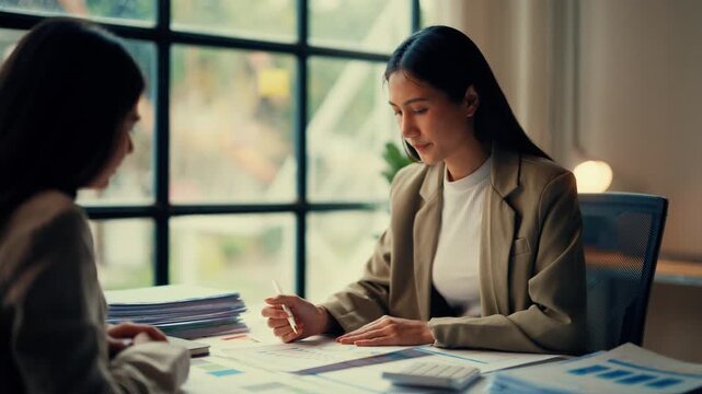 Two professional businesswomen collaborate on documents in a modern office, analyzing data and discussing business strategies