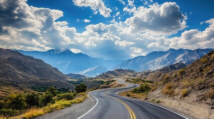 Fototapeta premium Road winding through mountains under a bright sky with fluffy clouds, creating a scenic and adventurous background with plenty of room for text.
