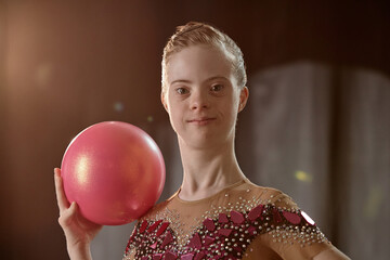 Portrait of young gymnast holding a shiny red ball and smiling at camera with confidence and joy...