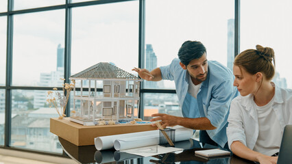 Smart architect engineer inspect house model while colleague using laptop analysis data. Professional designer team working together to design house model construction at modern office. Tracery