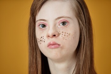 Portrait of young woman with Down Syndrome, looking straight at the camera Her face adorned with...