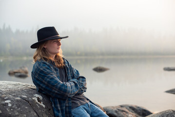 young man in flannel shirt and jeans, by forest mountain lake