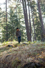 young man, wearing flannel shirt and jeans, walking though forest