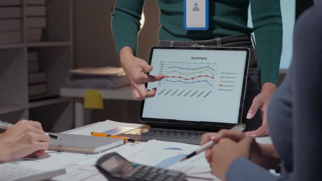 Professionals analyzing sales data on a tablet during a team meeting, focusing on charts and graphs to inform decisions