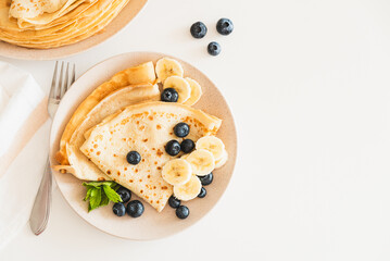 French crepes with banana and blueberries on white table. Top view