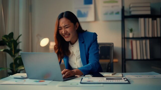 Businesswoman shows joy and triumph while working on her laptop in a professional office, displaying positive emotions like success and achievement