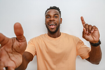 Young man enthusiastically gesturing with arms extended in a light-colored shirt against a neutral...