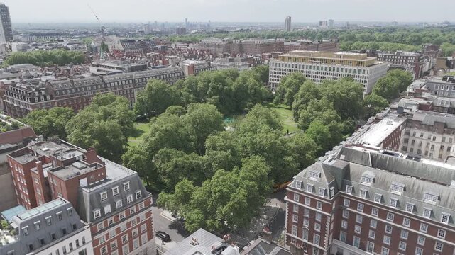 Aerial drone view of a green tree-covered park square in Central London, with period buildings surrounding it on a bright sunny day