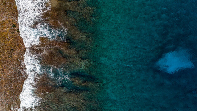 Aerial drone view looking down at south pacific ocean waves crashing into the shore of the tropical island Taha'a in French Polynesia. The azure, turquoise, blue water is deep and beautiful, 