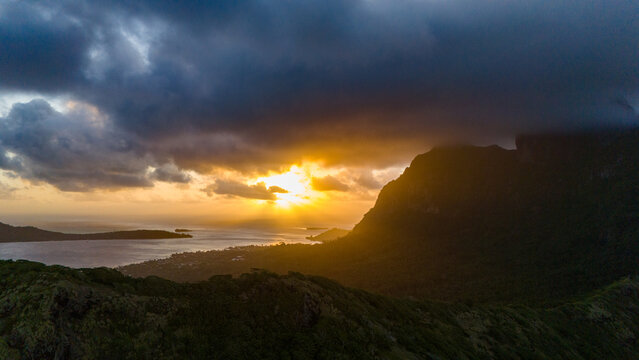 Dark clouds loom over Mount Otemanu on the tropical island Bora Bora. Aerial view by drone captures the sunset behind the large mountain and over the South Pacific ocean in French Polynesia. 