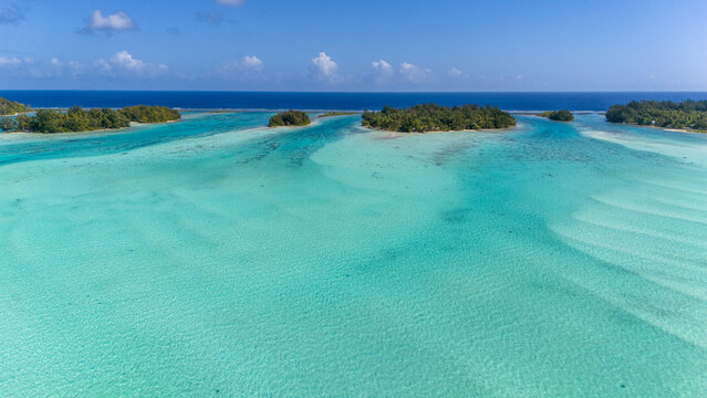 Beautiful azure blue south pacific ocean water surrounding small motu islands near the tropical island of Bora Bora in French Polynesia. Aerial view captured by drone. 