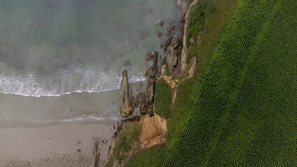 Aerial photograph overhead view of the beach with cliff by the sea, greenish-blue waters with a field of crops. Concept: Holidays, nature, wildlife.