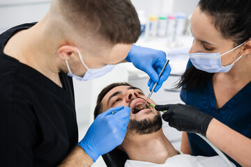 Handsome man is having preventive dental checkup in clinic. Initial examination of the patients...