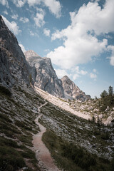 Obraz premium Rocky mountain trail leading toward dramatic peaks and blue sky.