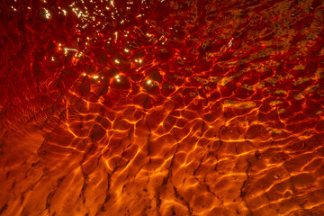 Close-up view of sunlight reflecting on rippling water, creating a vibrant display of red and...