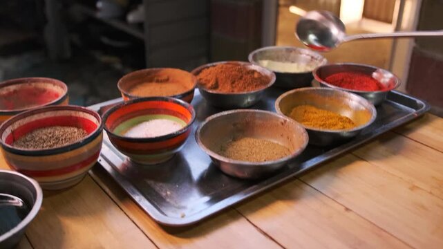Man's hand scoops up portions of spices and seasonings with a steel ladle: black pepper, paprika, turmeric, cumin, to prepare real Uzbek pilaf. Close up.