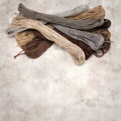 textured stylish old paper background, square, with cotton embroidery thread hanks in different...