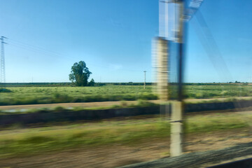 Nice moving view of a very green and lush countryside landscape with blue sky from the window of a speeding train in Spain