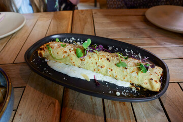 Stewed beef rib cannelloni with scattered parmesan cheese and cream sauce on a black tray on the table in a restaurant or at home