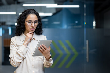 Focused businesswoman using tablet in modern office space. Analyzing data, making decisions, and...