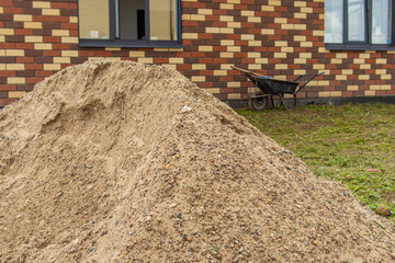 Pile of sand and gravel mixture and garden wheelbarrow on background. Material for work on the land...