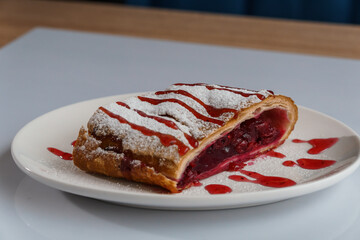 Dessert strudel with cherry and ice cream on a white plate