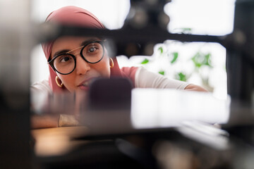 A woman in a dark red hijab examines the results of a 3D printing project, showcasing her attention to detail and the precision required in handling advanced technology.