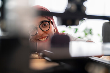 A woman in a dark red hijab examines the results of a 3D printing project, showcasing her attention to detail and the precision required in handling advanced technology.