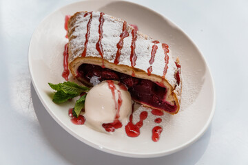 Dessert strudel with cherry and ice cream on a white plate