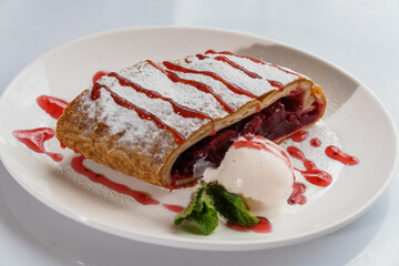 Dessert strudel with cherry and ice cream on a white plate