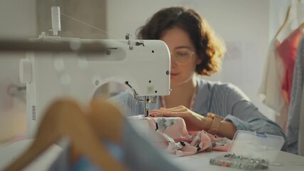 Workshop. Active woman in working uniform carefully using sewing machine in studio. Cinematic shot of fashion designer sewing new dress model new methods of sewing clothes, sample