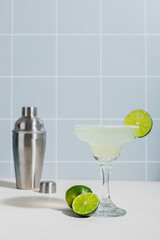 classic margarita cocktail with lime. Checkered tile background. Silver cocktail shaker in the background.