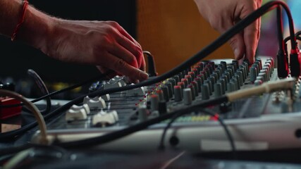 Sound engineer adjusting the settings on the mixing console during the daytime music performance, moving knobs and faders with the hands close up