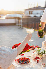 Romantic dinner on the rooftop at sunset. A man pours sparkling wine into a glass