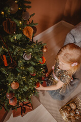 A girl in a sparkling dress decorates a Christmas tree