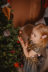 A girl in a sparkling dress decorates a Christmas tree