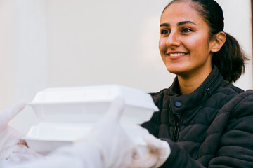 middle eastern delivery man wearing face mask in handling bag of food, fruit, vegetable give to female customer in front of the house. express grocery delivery service