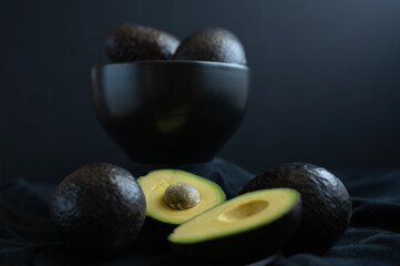 Avocados in a black bowl and on a table cloth.