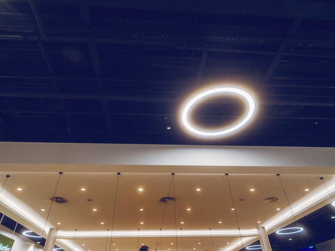 Fototapeta A ceiling with a large circle light hanging from it. The light is lit up and the room is dark. Modern LED illumination. Efficient and economical texhnology.