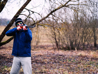 A man in a blue jacket is holding a shotgun. The image has a mood of excitement and anticipation,...