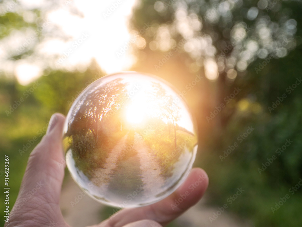 Wall mural a person is holding a clear glass ball that is reflecting the sunrise over a small country road, sel
