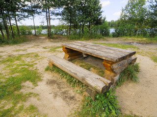 Wooden table and bench in a picnic area of a public park. Hand made design and craft. Forest in the background. Public area for rest and food consumption