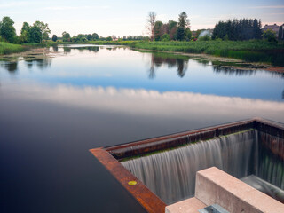 A small waterfall is flowing into a pool from a dam on a small river. The water is clear and calm, and the pool is surrounded by trees. Concept of tranquility and natural beauty.