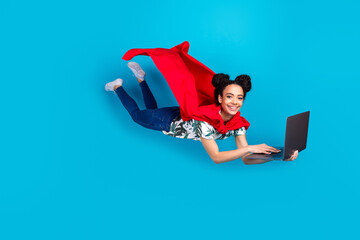 Full body portrait of lovely young girl superhero costume fly laptop isolated on blue color background © deagreez