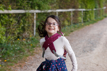 Little girl with glasses and a backpack in the forest. Little traveler on a hike. Concept of...