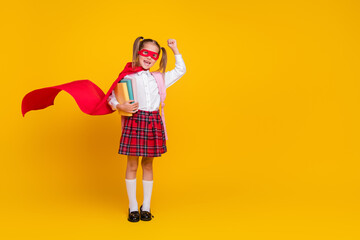 Full body portrait of little schoolkid superhero costume uniform book raise fist isolated on yellow color background