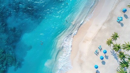 Fototapeta premium An aerial view shows a sandy beach with blue umbrellas and palm trees on the shore of a tropical island