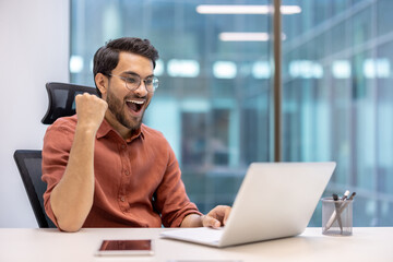 Young man celebrating successful achievement while working on laptop. Joyful professional feeling...