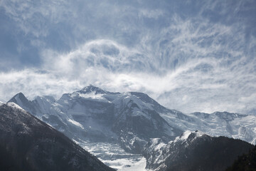 Obraz premium Snow-capped mountains rise above a valley with swirling clouds, creating a majestic and awe-inspiring landscape perfect for adventure and exploration