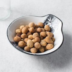 Fried coated peanuts in a white ceramic plate, cracker peanuts on a marble countertop, nigerian peanut snack in a small white plate